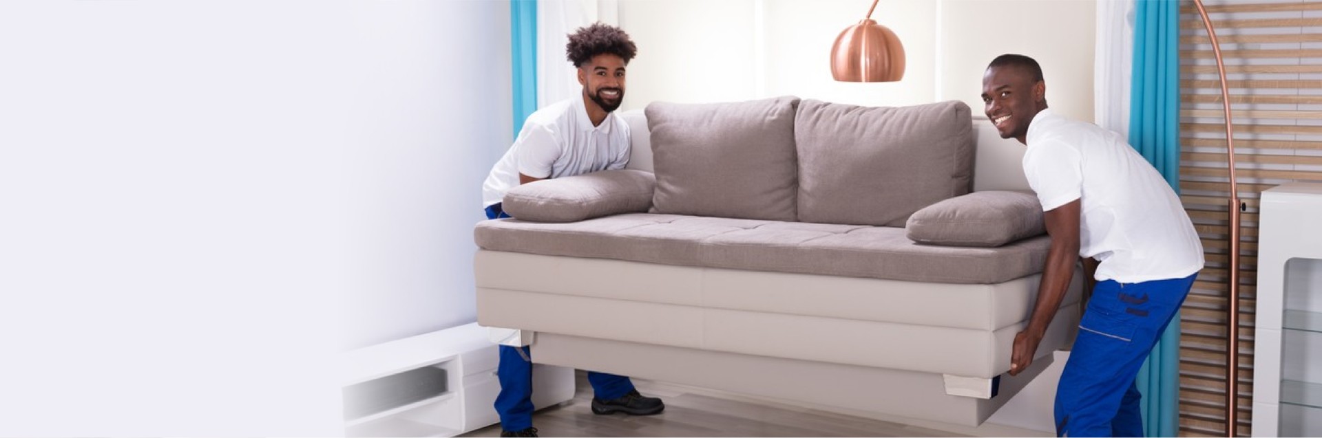 Two Young Male Movers In The White Uniform Placing The Sofa In The Living Room