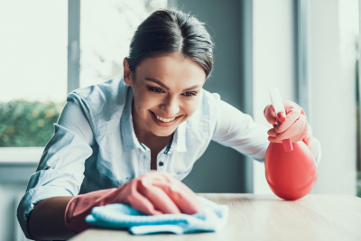 Young Smiling Woman in Gloves Cleaning House. Happy Beautiful Girl wearing Protective Gloves Cleaning Desk by spraying Cleaning Products and wiping with Sponge. Woman Cleaning Apartment