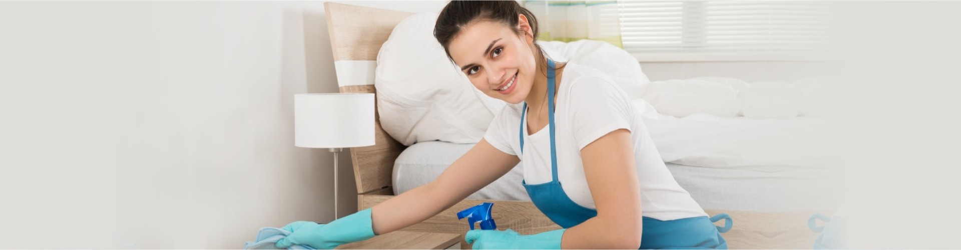 Happy Female Housekeeper Cleaning Nightstand In Room