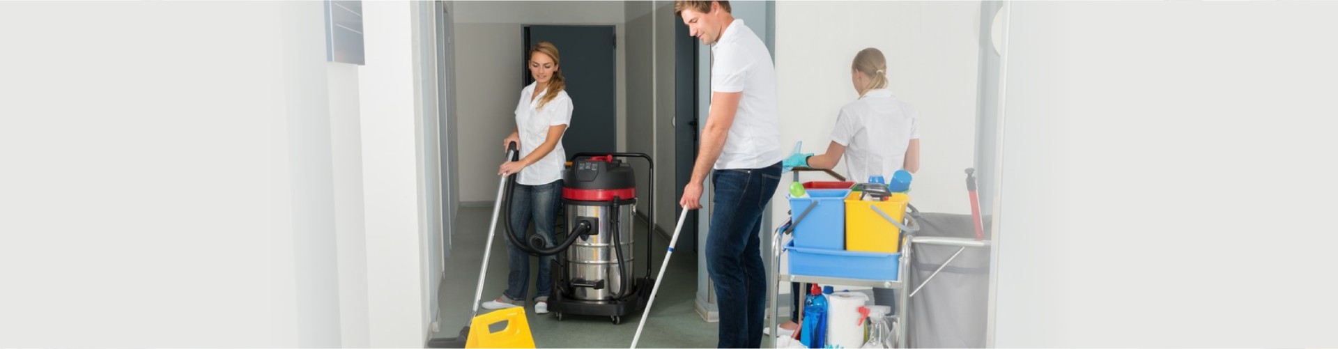 Group Of Janitors Cleaning Floor In Corridor With Caution Sign